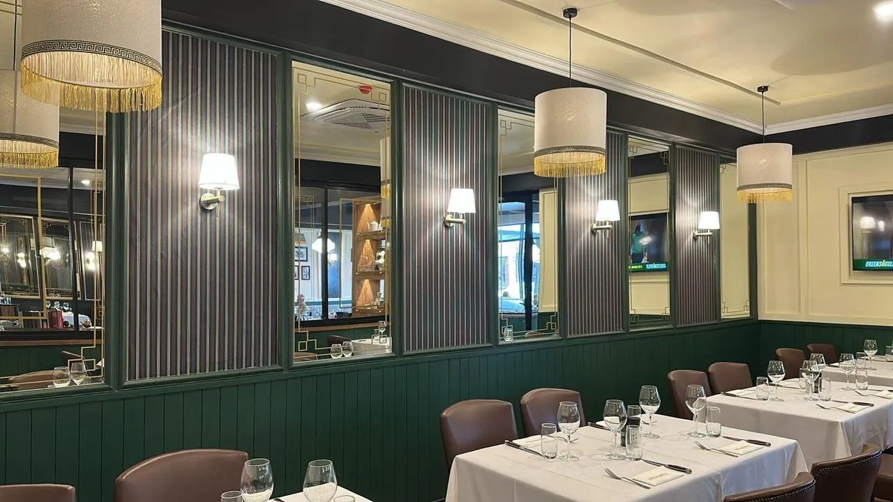 A Hussar Grill dining room: green panelled walls, white linen and brass lamps